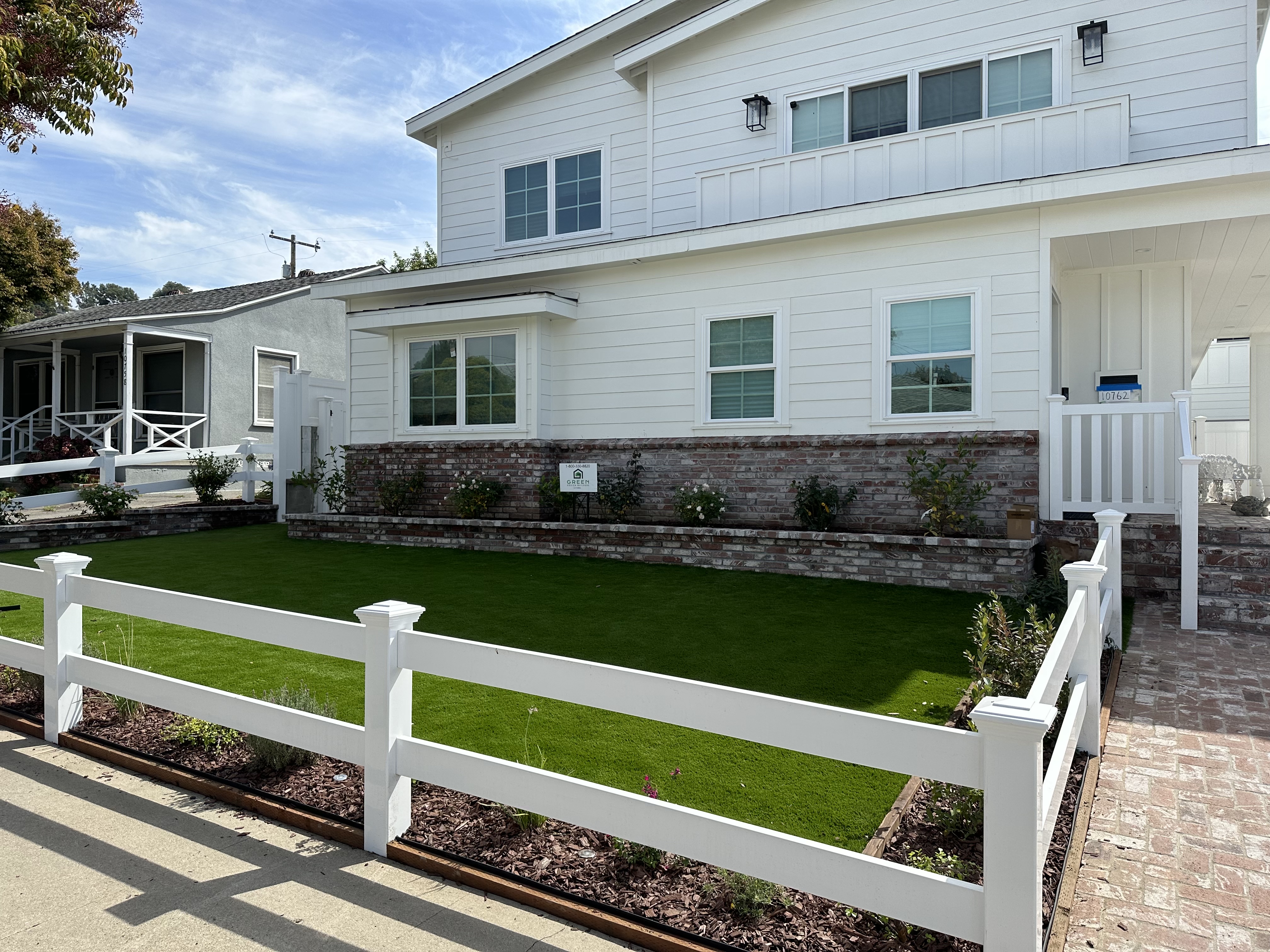 A picture showing turf and a white fence with a white house